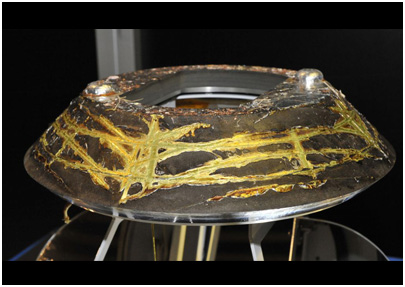 宇宙から帰還したヒートシールドの背面。背面側の加熱からカプセルを守るとともに、パラシュート開傘時には、パラシュートを引き出す役目もする。カプセル単体で飛行している時の温度を解析しやすくするため、アルミを蒸着したカプトンテープが貼付けてあったが、再突入時の高温でテープは燃えてしまった。表面の模様はテープの燃え残りである。